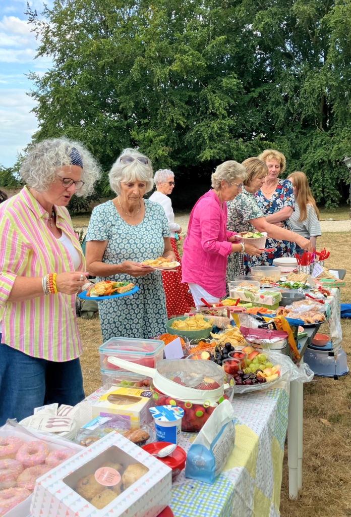 Little Lifts breast cancer charity supporters serving themselves from a table of sandwiches, salads and baked treats at a community garden party.
