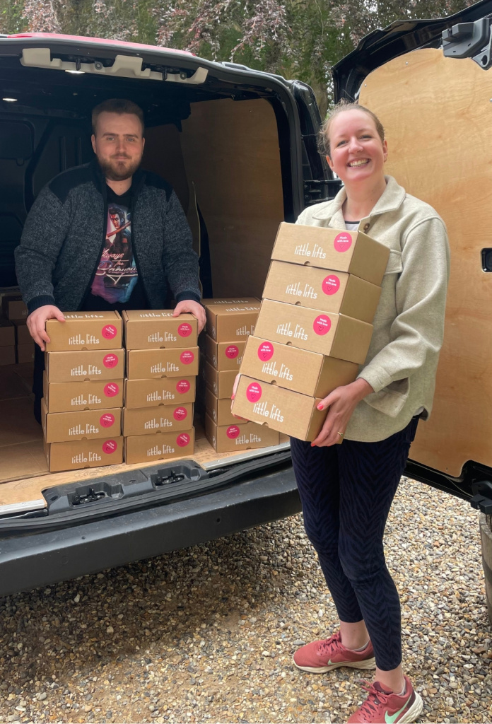 George in the back of a van loaded with Boxes, alongside a colleague holding a stack of Boxes