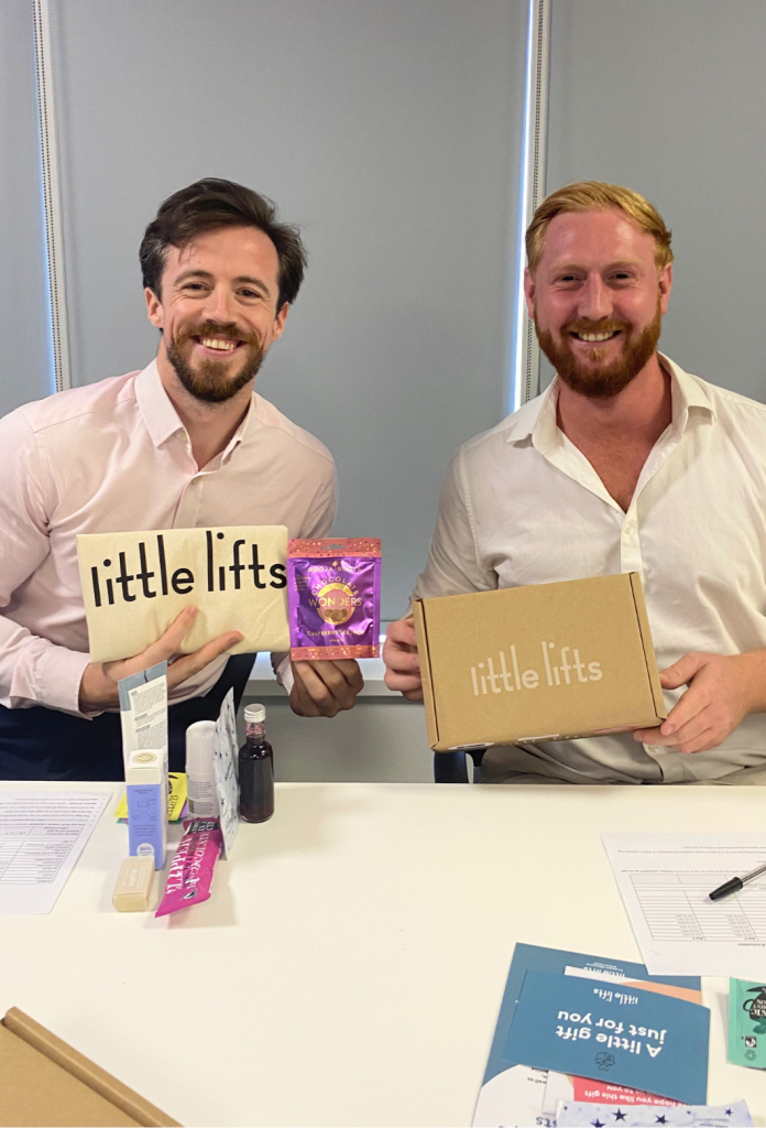 Two New Homes Group colleagues holding a Little Lifts box and gift items for breast cancer patients.