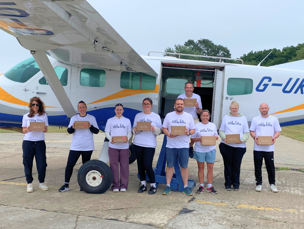 Little Lifts fundraisers standing in front of an aeroplane, holding Little Lifts Boxes ahead of their skydive.