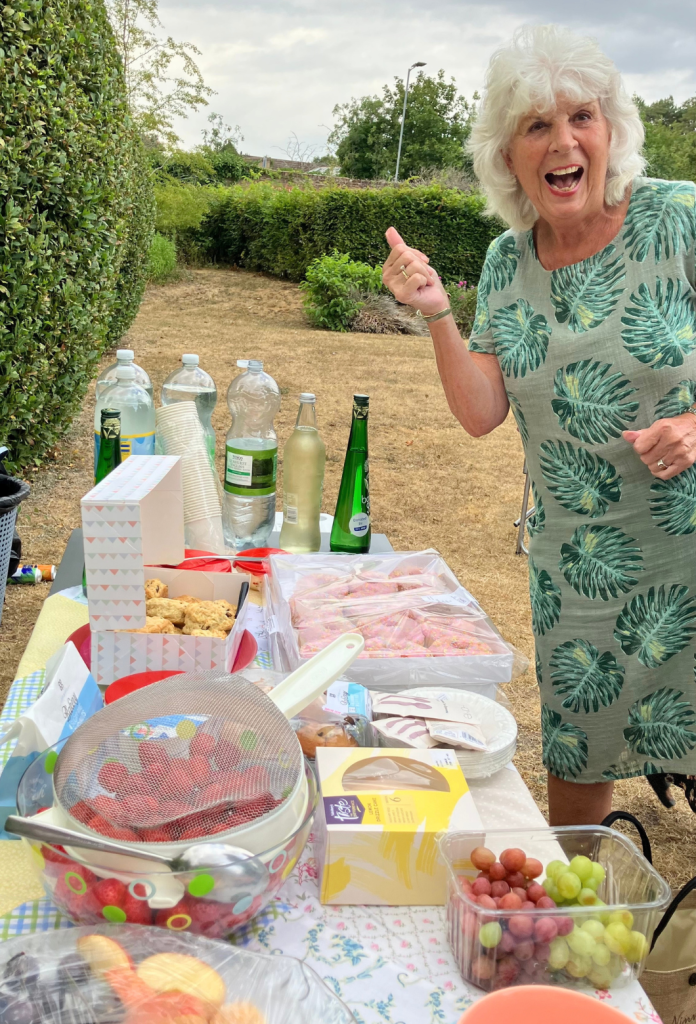 A Little Lifts breast cancer charity supporter celebrating at an outdoor event, with drinks, scones and strawberries on the table.