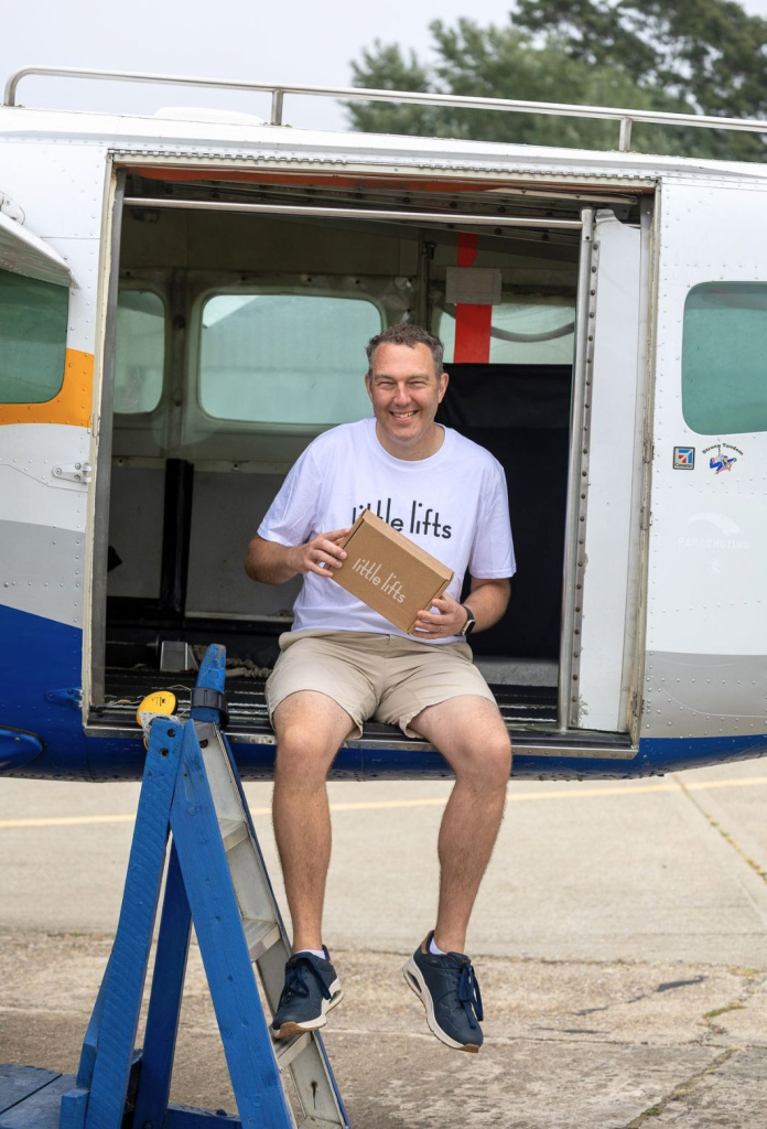 Michael sitting in the open door of the skydiving plane, holding a Little Lifts breast cancer charity Box before his jump.